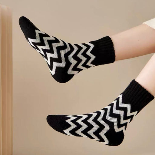 Feet wearing black and white zigzag socks with legs raised against neutral background