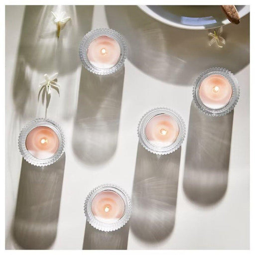 Candle holders with small candles on a white surface with plant shadows