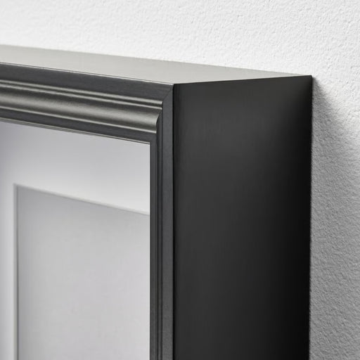 Close-up of a black framed mirror corner on a white wall.