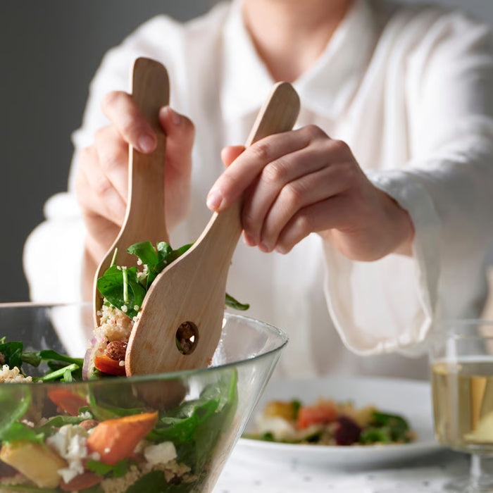 Person using wooden salad servers to serve a salad with a blurred background