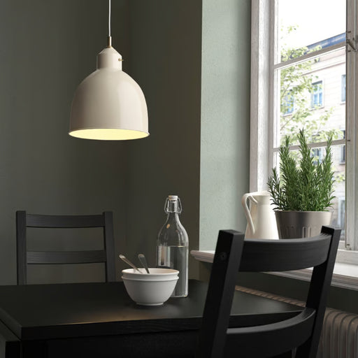Light beige RÖDFLIK pendant lamp hanging over a black dining table, providing a focused and warm downward glow.