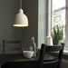 Light beige RÖDFLIK pendant lamp hanging over a black dining table, providing a focused and warm downward glow.