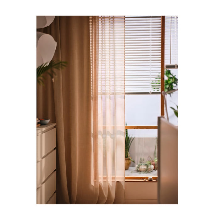 Sheer beige curtain in front of a window with blinds, interior decor.