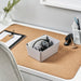 Organized desk setup featuring a light grey upholstered chair, a cork mat, a white storage box holding various desk essentials, and a mesh pen holder with stationery—ideal for workspace organization.-20599149