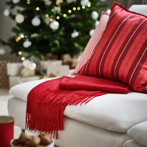 VINTERFINT throw draped over white seating with red pillows, adding warmth and holiday charm beside a Christmas tree