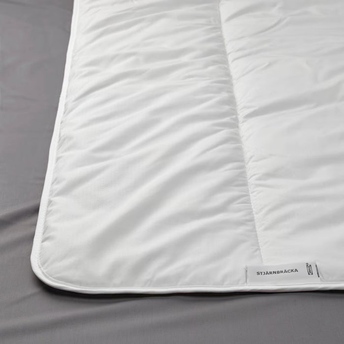 Close-up of IKEA STJÄRNBRÄCKA warm white duvet, 150x200 cm, showing stitched pattern and product label on corner; placed on grey surface – 00458089