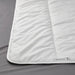 Close-up of IKEA STJÄRNBRÄCKA warm white duvet, 150x200 cm, showing stitched pattern and product label on corner; placed on grey surface – 00458089