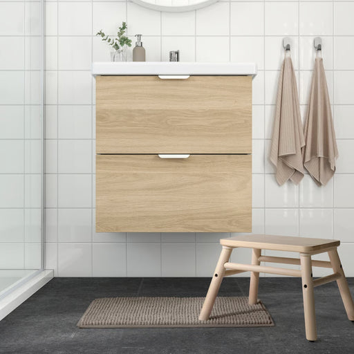 IKEA TOFTBO bath mat placed in a Scandinavian-style bathroom with light wood vanity, beige towels, and dark tile flooring