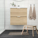 IKEA TOFTBO bath mat placed in a Scandinavian-style bathroom with light wood vanity, beige towels, and dark tile flooring