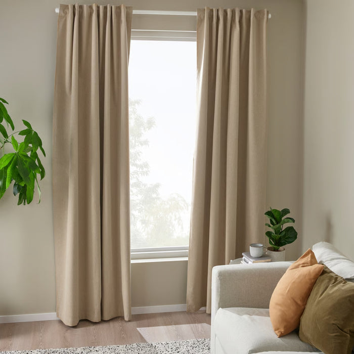 Beige curtains in a room with a white sofa, cushions, and a plant.