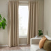 Beige curtains in a room with a white sofa, cushions, and a plant.