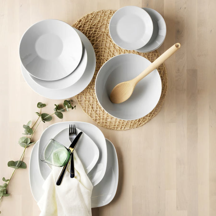 Set of white ceramic plates with a wooden spoon and cutlery on a woven placemat.