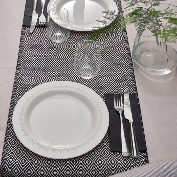 Table setting with white plates, silverware, and a geometric black and white placemat.