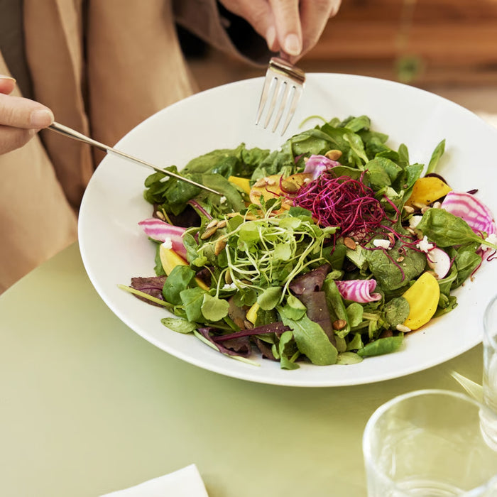 Person holding a fork over a plate of colorful salad on a table.