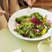 Person holding a fork over a plate of colorful salad on a table.