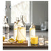 Glass bottles with lemon slices on a kitchen counter with a glass of orange juice.