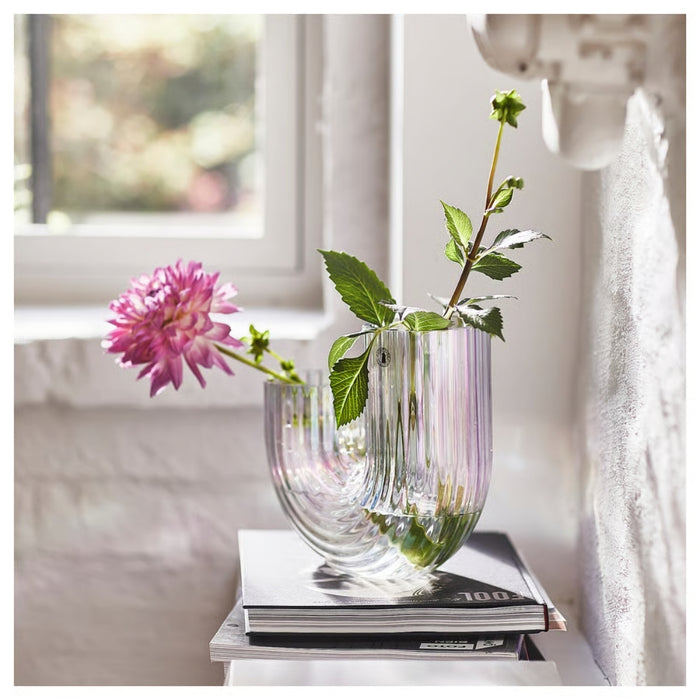 Glass vase with pink flower and green leaves on a stack of books in a softly blurred indoor setting