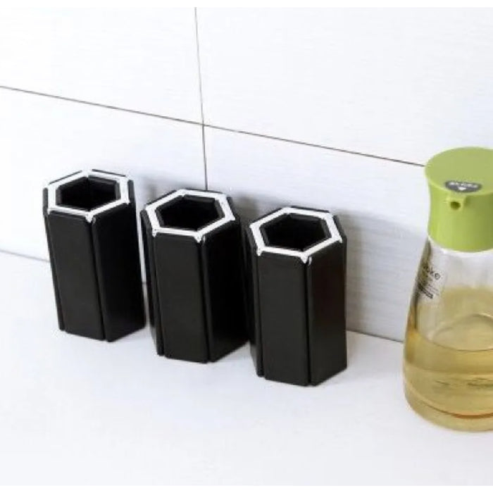 Three black hexagonal bottles against a tiled wall with a bottle of yellow liquid nearby.