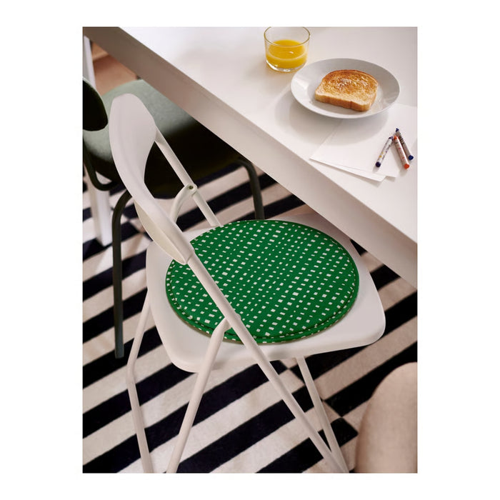 White chair with a green cushion on a black and white striped rug, with a table and food in the background.
