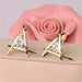 Triangle gold earrings – round crystal in intersecting gold triangle frame, placed on soft fabric with pink rose backdrop

