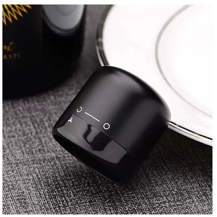 A close-up of a small matte black cylindrical electronic device with white control icons, resting on a textured gray surface next to a white plate.