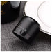 A close-up of a small matte black cylindrical electronic device with white control icons, resting on a textured gray surface next to a white plate.
