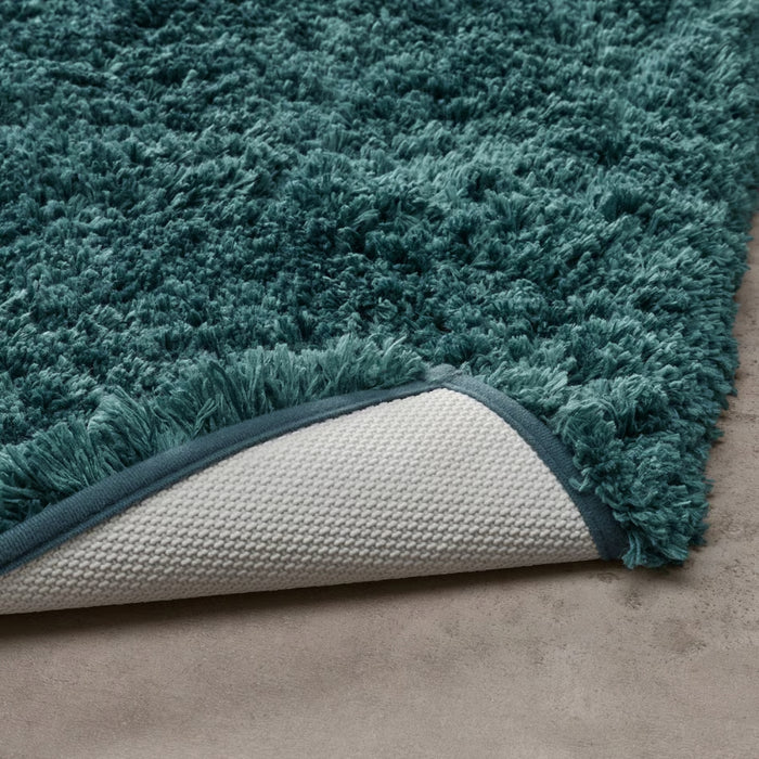 Teal rug with textured border on a neutral background