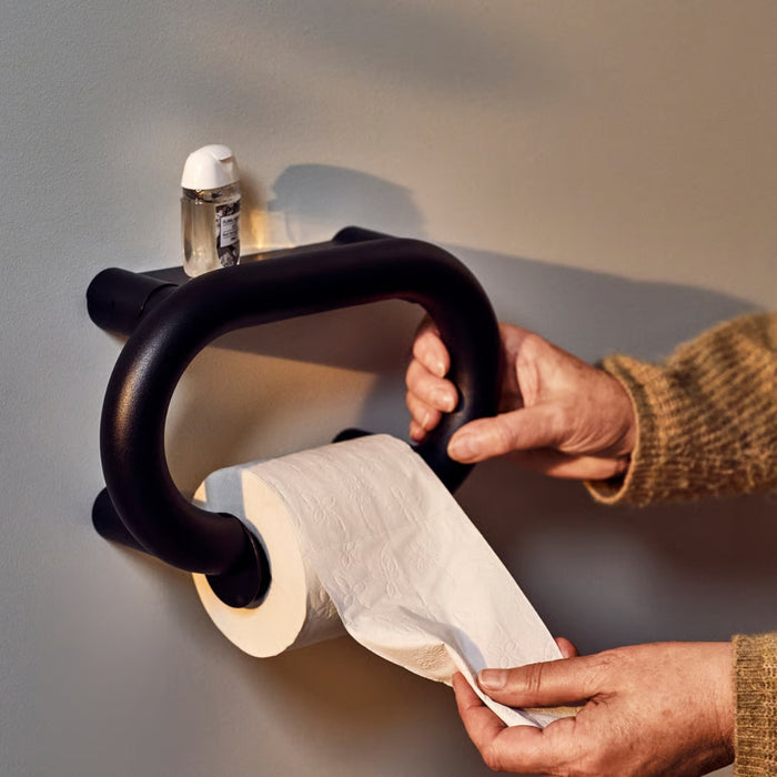 Person using a black wall-mounted paper towel holder with a roll of paper towels.
