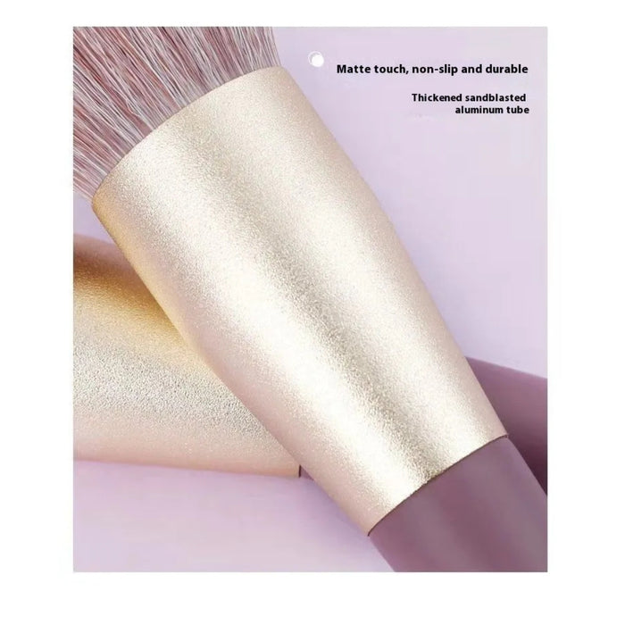 Makeup brush with gold and purple handle on a light pink background