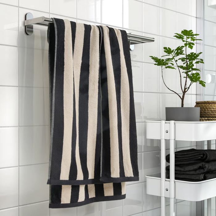 Black and beige striped towel hanging on a rack in a bathroom with a plant and folded towels on a shelf.