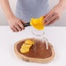 Person using a yellow citrus squeezer over a glass pitcher with lemon slices on a wooden board.