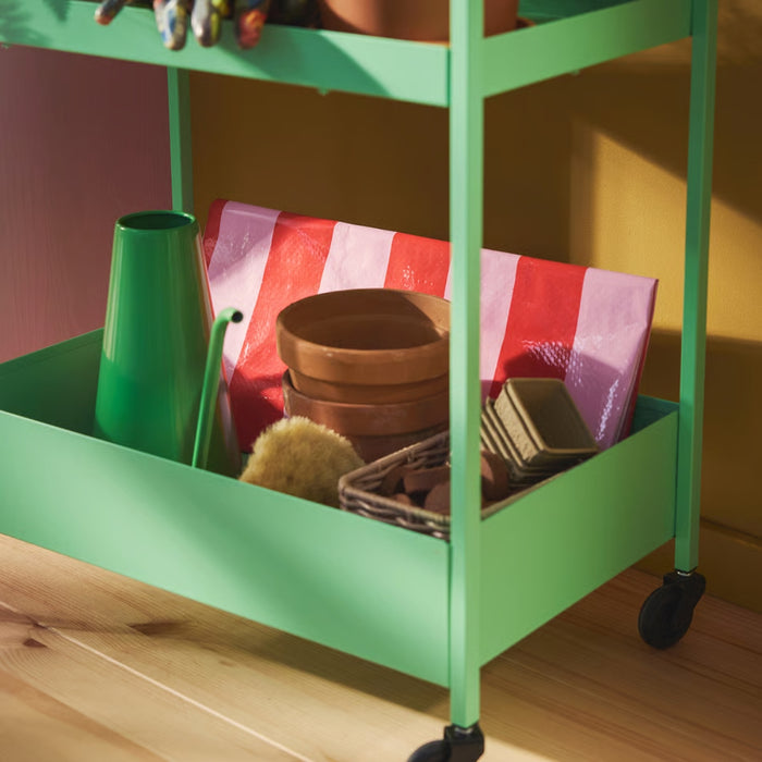 Folded IKEA DOFTRIPS gardening mat stored neatly on a green rolling utility cart alongside flower pots.
