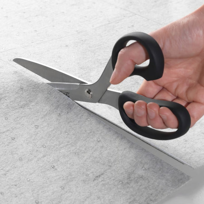 Hand holding a pair of scissors cutting gray paper on a light gray background