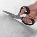 Hand holding a pair of scissors cutting gray paper on a light gray background