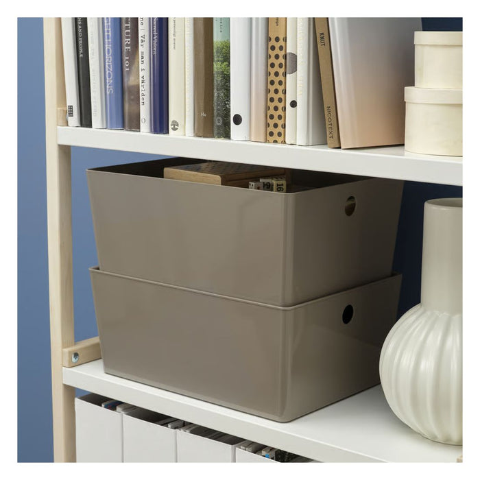 Two beige storage boxes on a white shelf with books and containers.