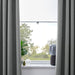 Gray curtains partially drawn to reveal a window with a view of greenery outside.