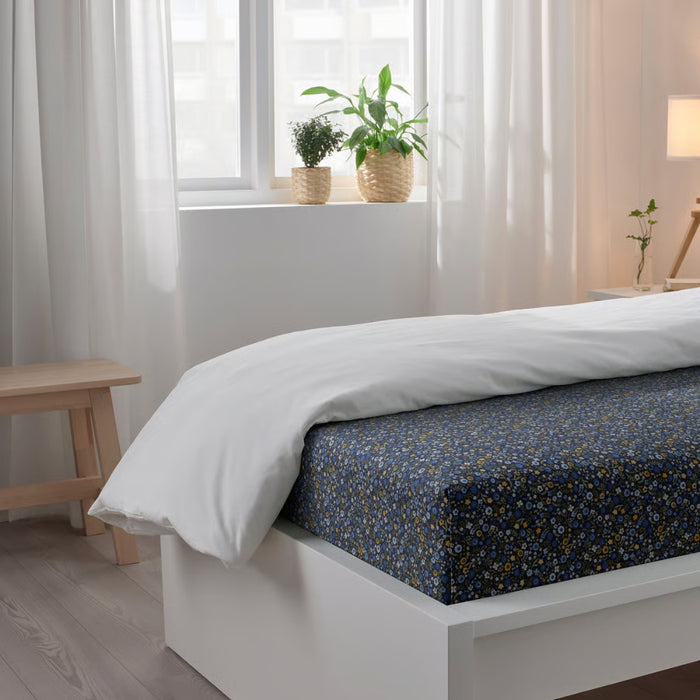 Bed with white duvet and blue floral patterned sheets in a bright bedroom.