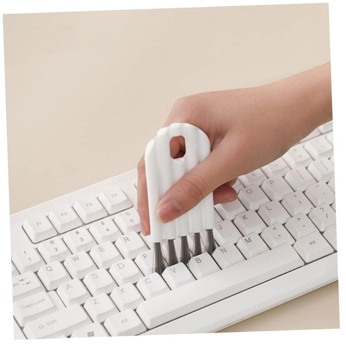 Hand using a white keyboard cleaning brush on a computer keyboard.