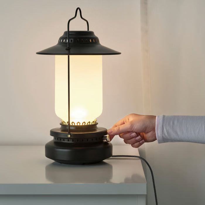 Hand plugging in a black lantern-style lamp on a white surface with a neutral background