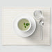 Cup of green tea with a mint leaf on a white saucer, placed on a light wooden placemat.