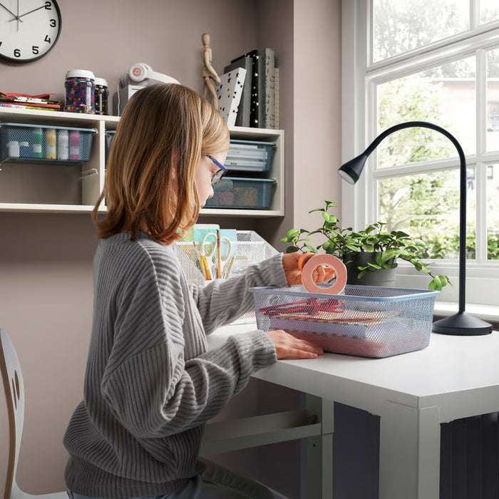 Child organizing craft materials at a white desk using TROFAST mesh box, surrounded by stationery and pink tape