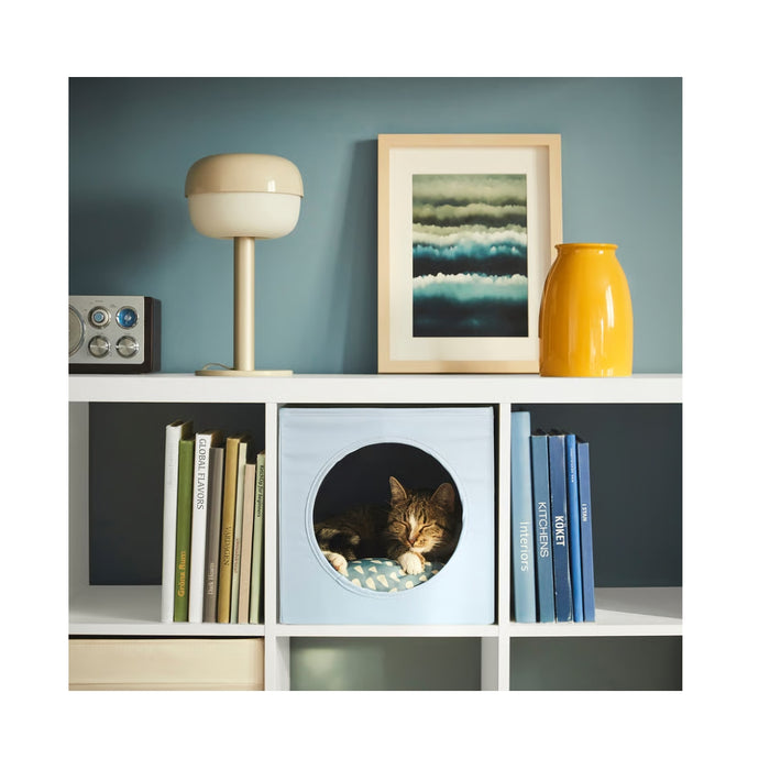 UTSÅDD cat house, grey-blue, 33x38x33 cm – cube with circular opening, placed in KALLAX shelf. Cat resting inside on patterned cushion. Cozy and stylish – 50572105.