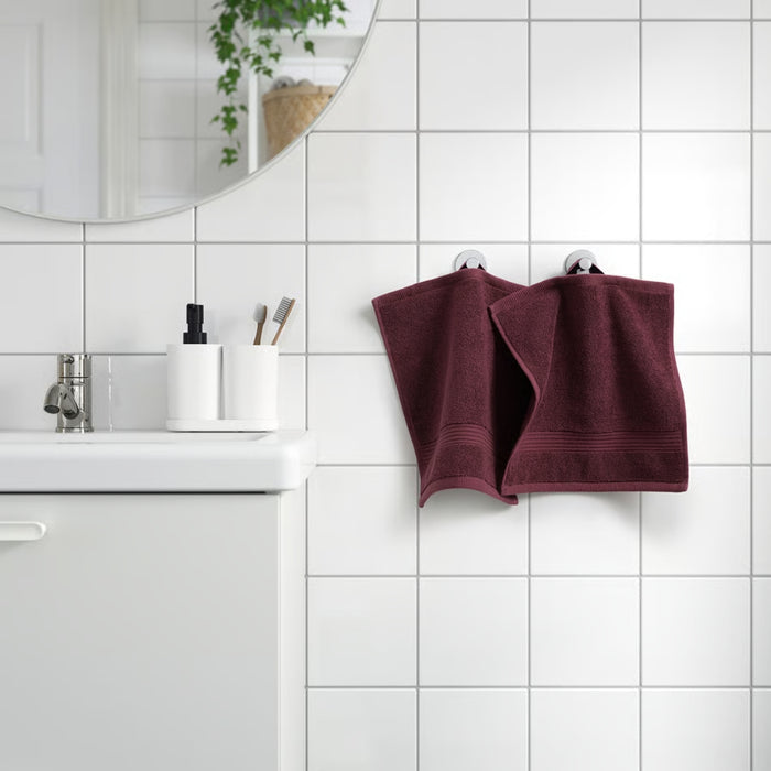 IKEA FREDRIKSJÖN washcloth in deep red, 30x30 cm (12x12"); shown hanging on white tiled bathroom wall beside matching towel – styled with round mirror, white sink, and green plant for elegant, color-coordinated decor - 70552762