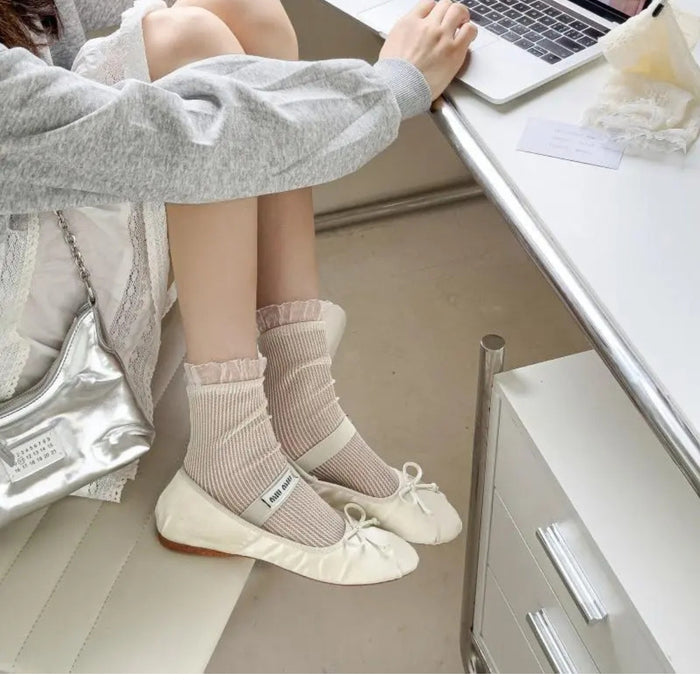 Person sitting at a desk wearing light-colored socks and white shoes, with a laptop on the desk.