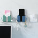 Blue and green wall-mounted holders on tiled wall; green holder contains a small colorful item, blue holder holds a black smartphone connected to a white charging cable and earphones—placed above a computer monitor for organized charging setup – 1598448185067 13069398.