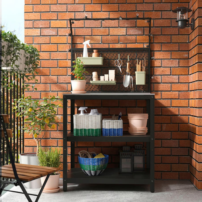 A well-organized outdoor gardening station with a black metal shelving unit against a brick wall. The shelves hold woven baskets in green, blue, and white filled with gardening tools, spray bottles, and terracotta pots.-10591422