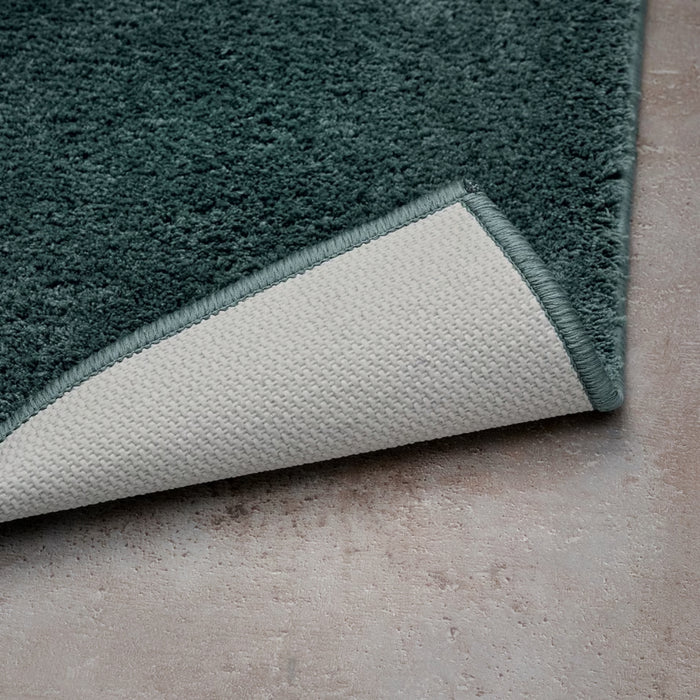 Close-up of a Turquoise Bathmat with a white border on a concrete floor.
