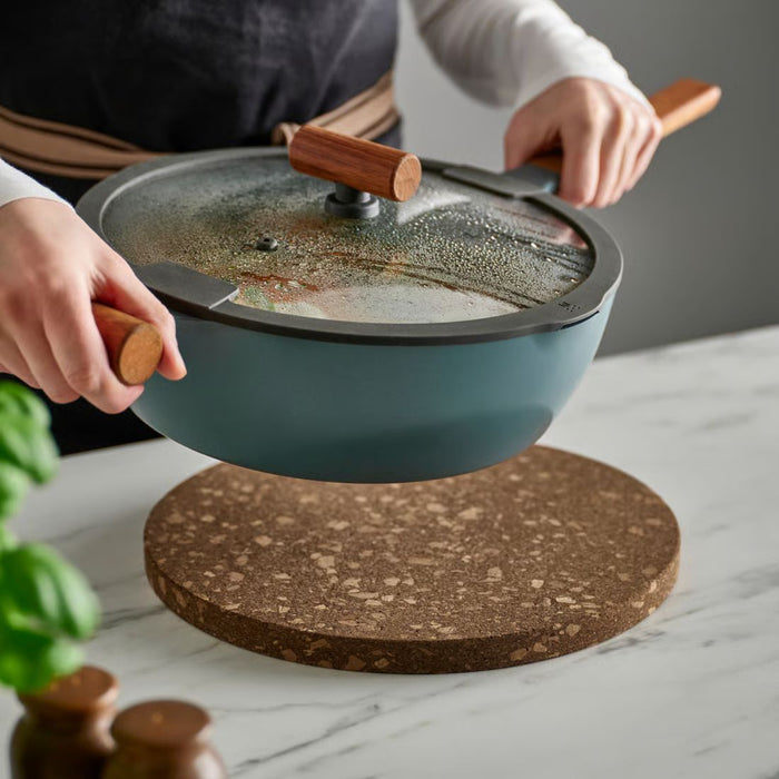 Person holding a green frying pan with wooden handles on a marble surface