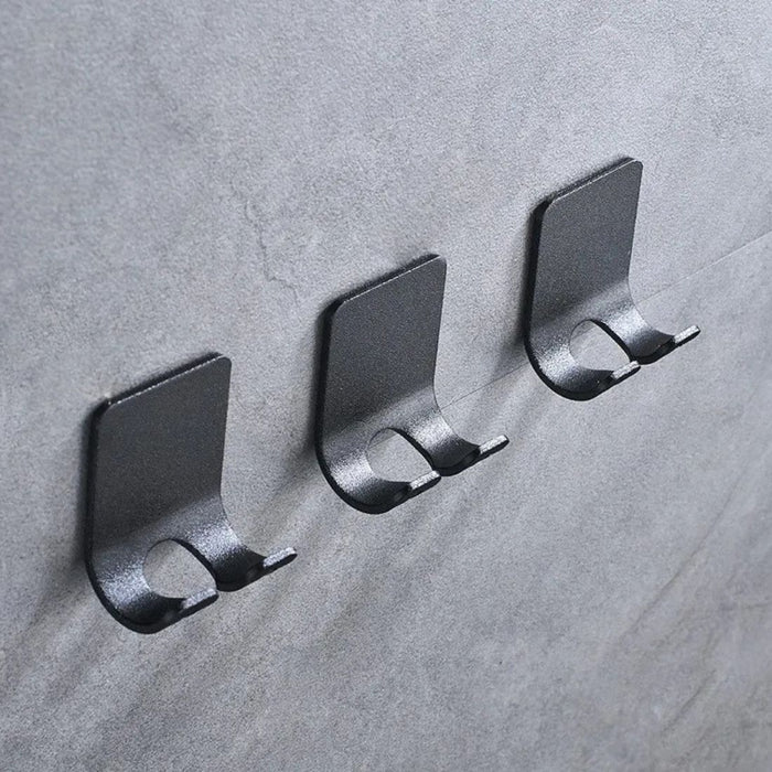 Three minimalist black wall hooks mounted on gray textured wall
