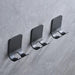 Three minimalist black wall hooks mounted on gray textured wall